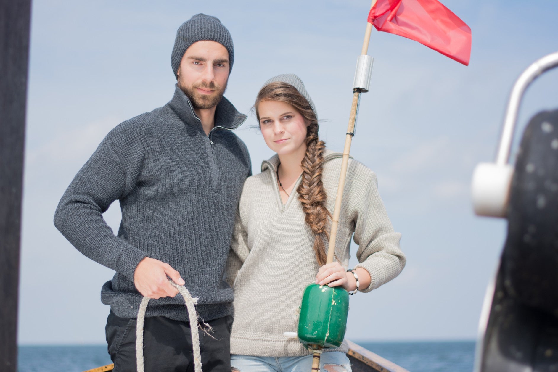 Paar mit maritimen Strickmützen und Seemannspullovern von Blauer Peter auf einem Boot – wärmende Outdoor-Mode für Wind und Wetter
