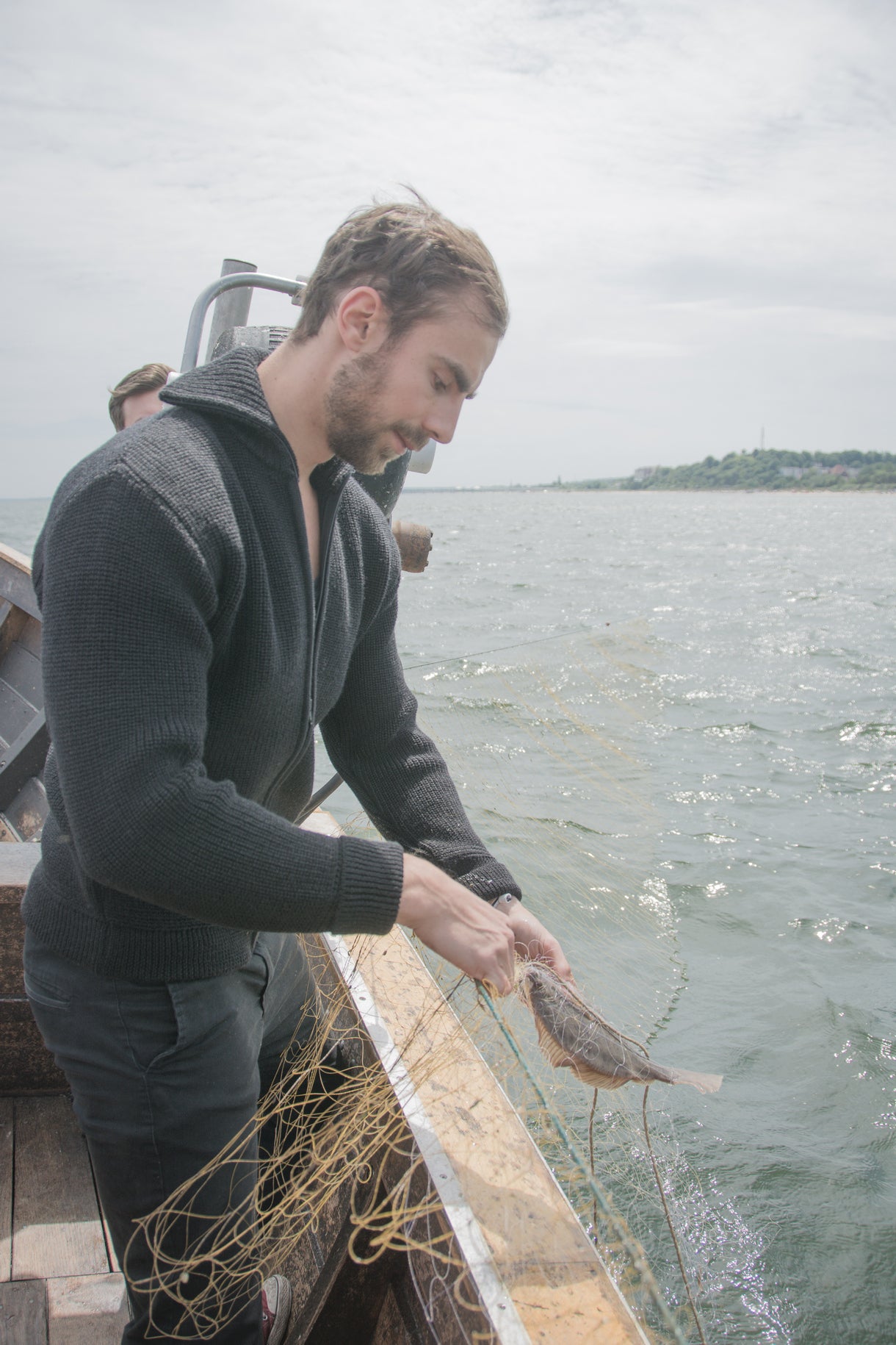 Mann im dunkelgrauen Seemanns-Troyer von Blauer Peter beim Fischen auf einem Kutter