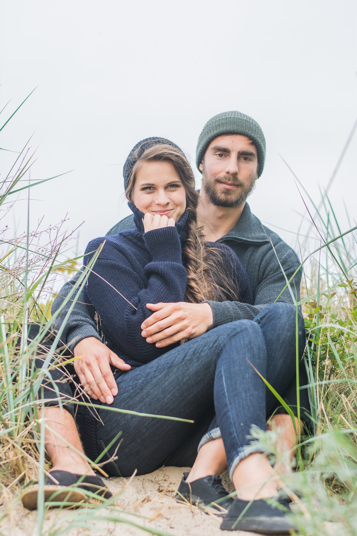 Paar in Seemannspullovern von Blauer Peter aus Merinowolle sitzt in Dünen am Meer – maritimer Outdoor-Look
