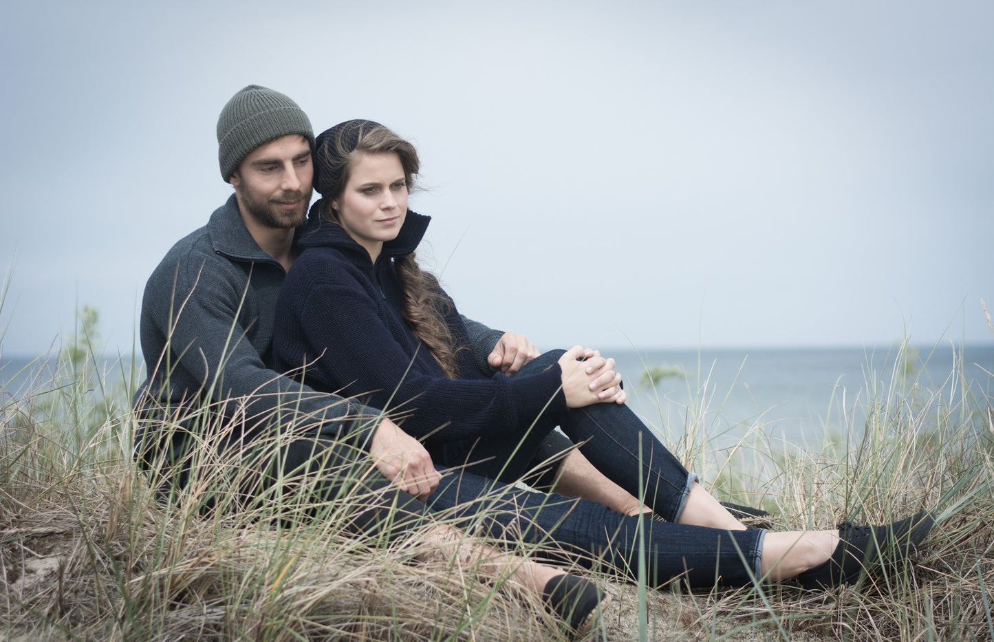 Paar in Seemannspullovern von Blauer Peter aus Merinowolle sitzt in Dünen am Meer – maritimer Outdoor-Look