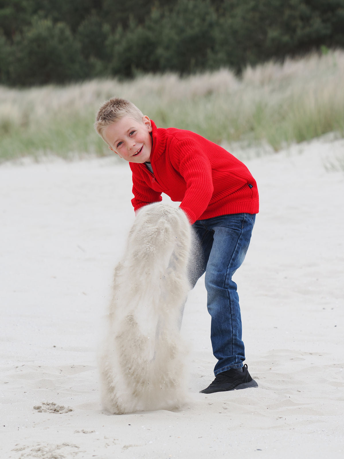 Junge spielt mit rotem Troyer im Sand