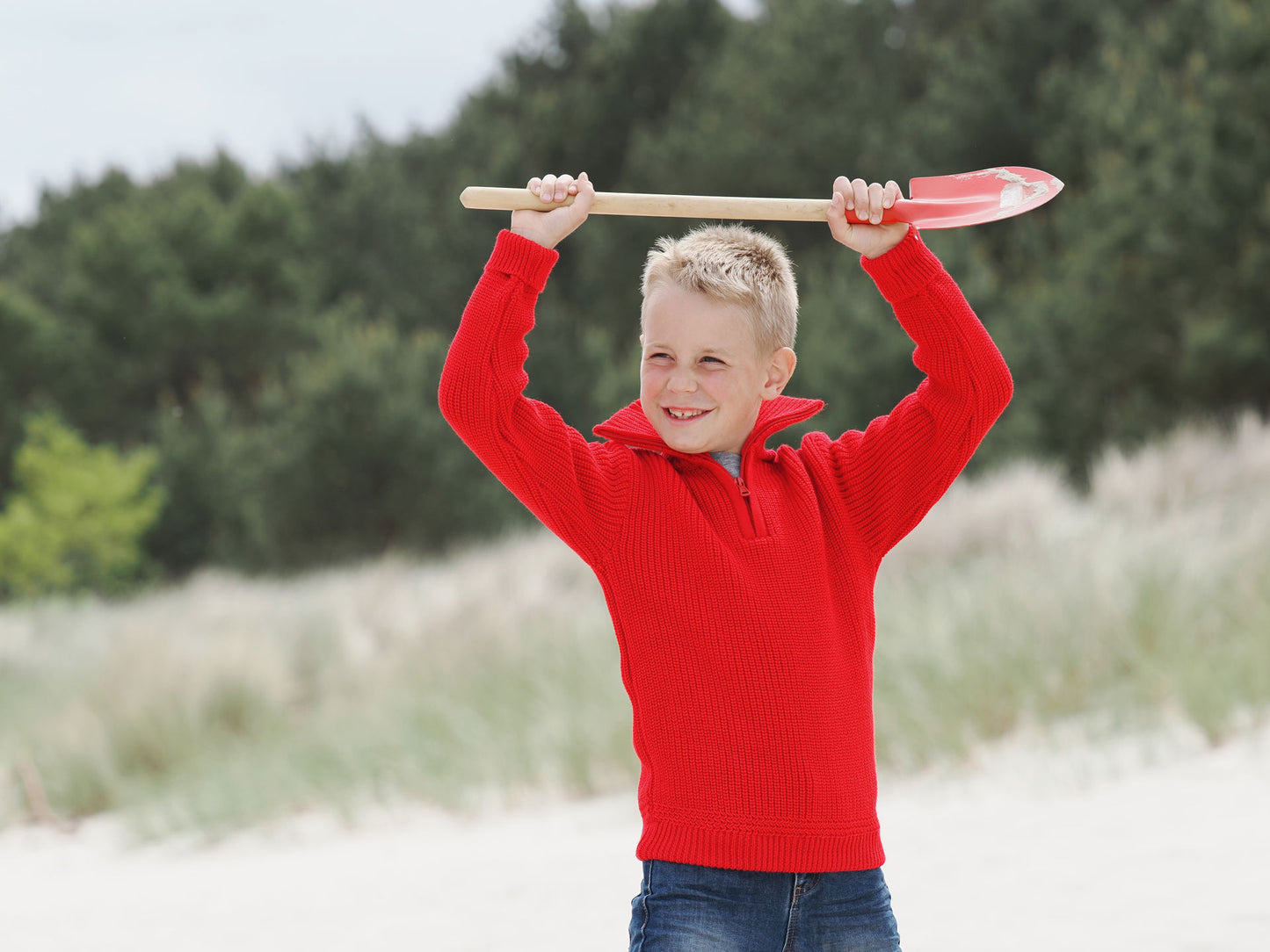 Junge spielt in rotem Kinder-Troyer von Blauer Peter mit Schaufel