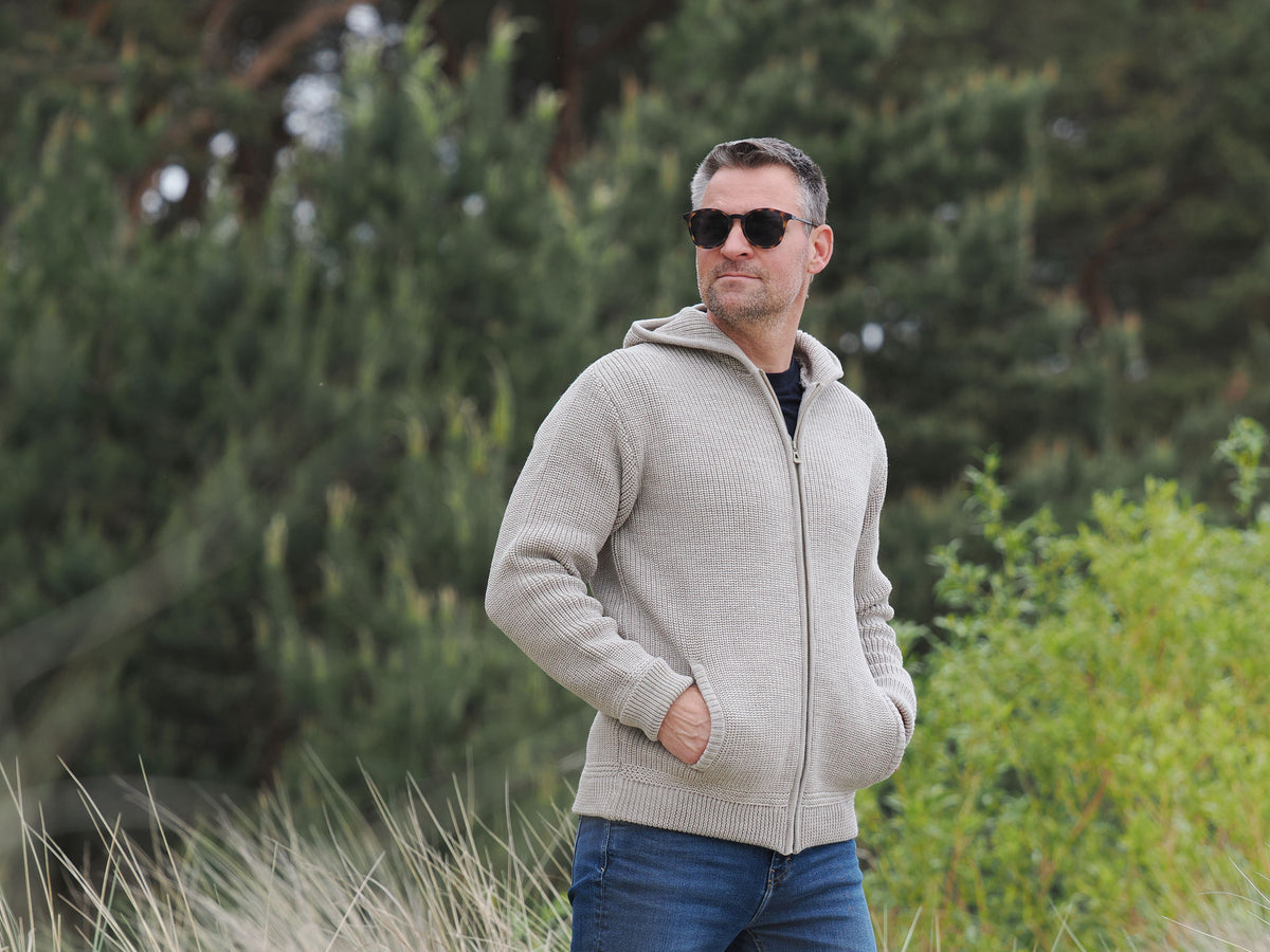 Mann trägt mit Kapuzen-Troyer-Jacke und Sonnenbrille in den Dünen