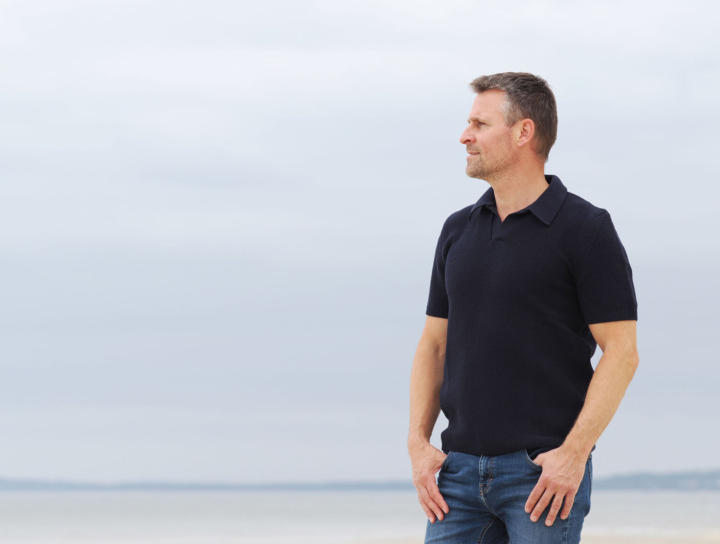Mann im marinefarbenen Strickpolo am Strand