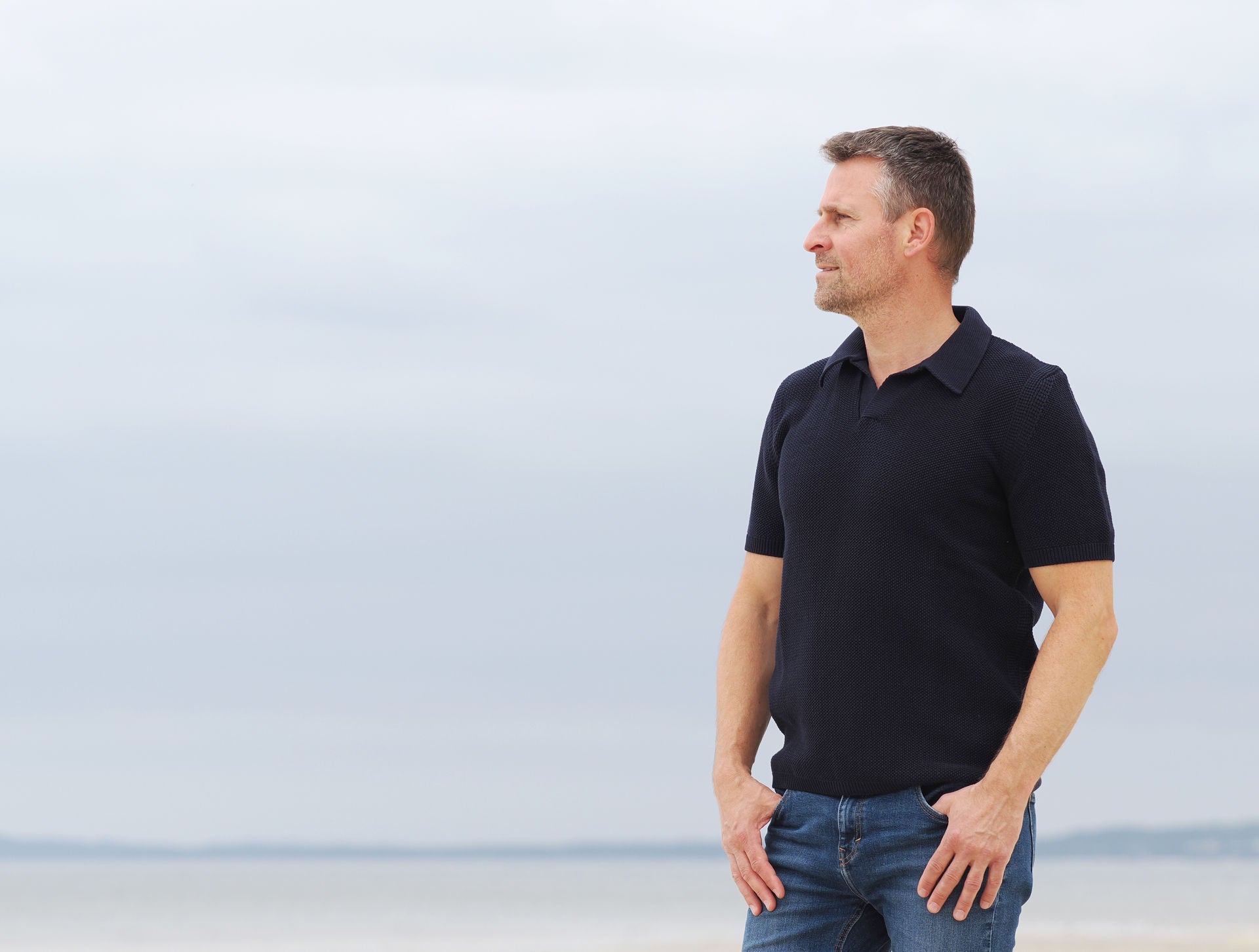 Mann im marinefarbenen Strickpolo am Strand