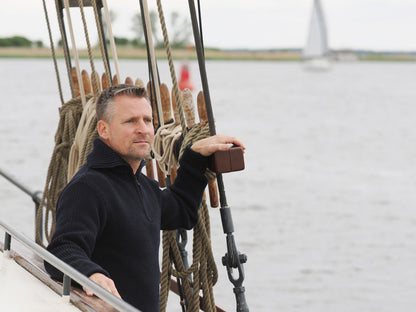 Mann steht mit Troyer an Deck und schaut aufs Meer