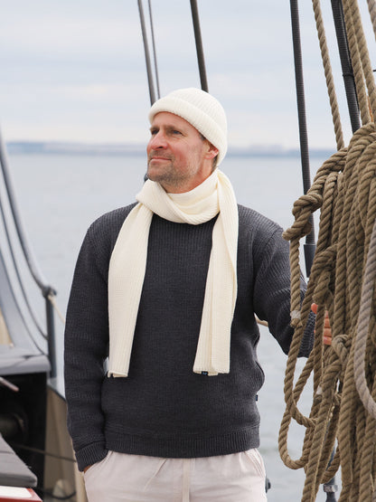 Mann mit Mütze und Schal an Deck schaut aufs Meer