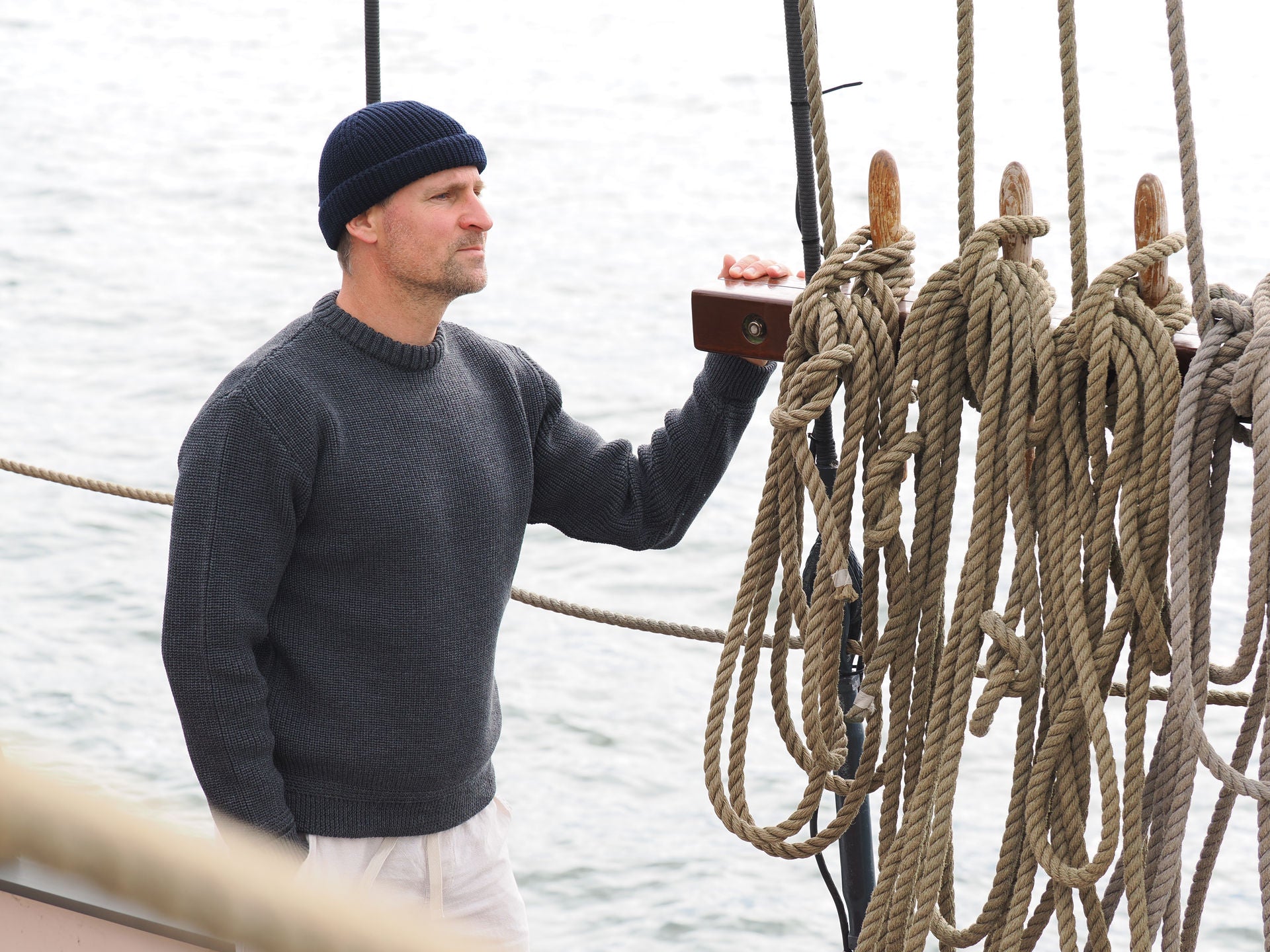 Mann schaut mit Rundhals-Troyer und Beanie-Mütze auf Schiff in die Ferne