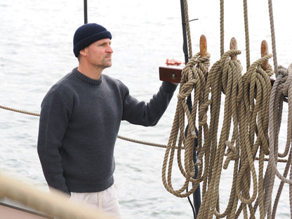 Mann schaut mit Rundhals-Troyer und Beanie-Mütze auf Schiff in die Ferne