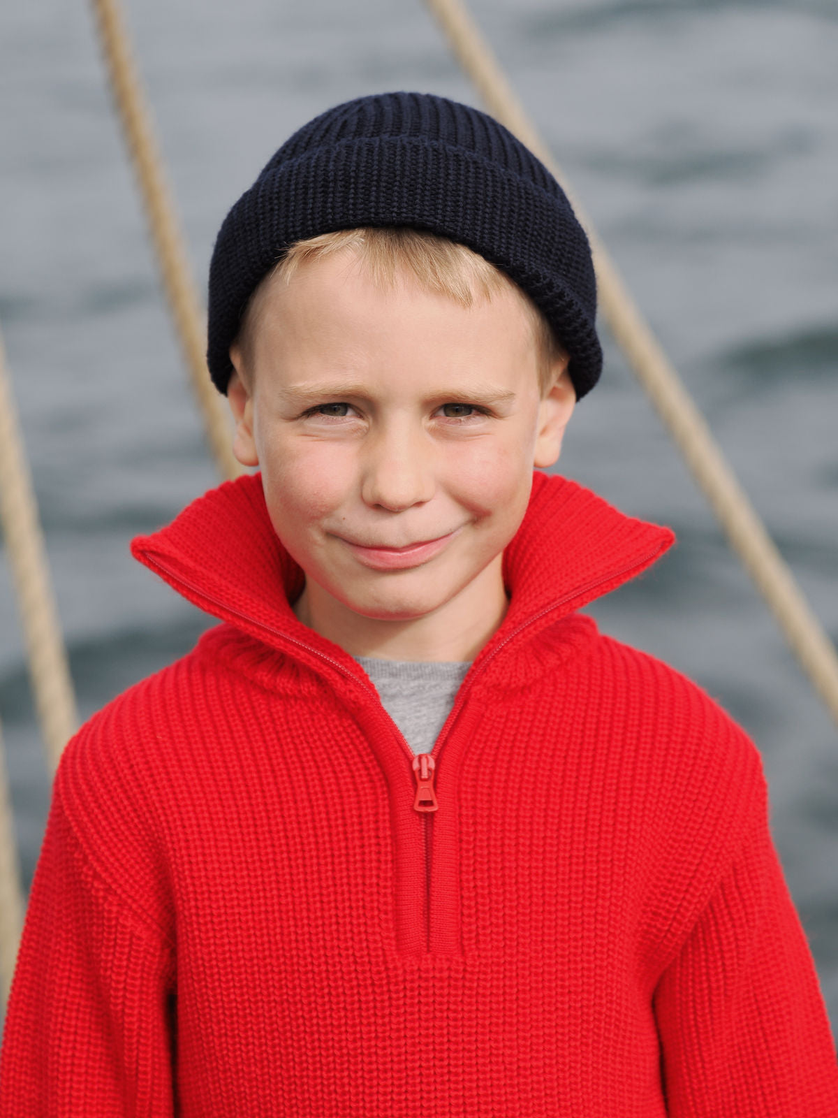 Junge mit rotem Troyer und blauer Strickmütze an Deck