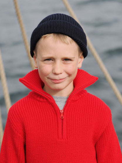 Junge mit rotem Troyer und blauer Strickmütze an Deck
