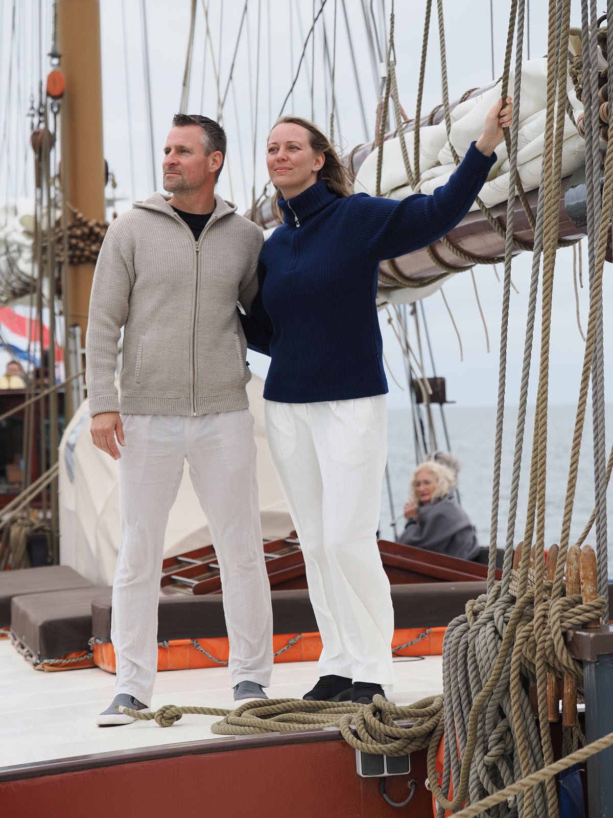 Paar steht in Kapuzen-Troyer-Jacke und Cashmere-Troyer an Deck eines Segelbootes