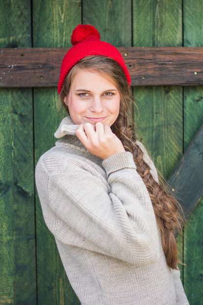 Junge Frau im beigefarbenen Schurwoll-Troyer und roter Strickmütze von Blauer Peter vor rustikalem Holzhintergrund