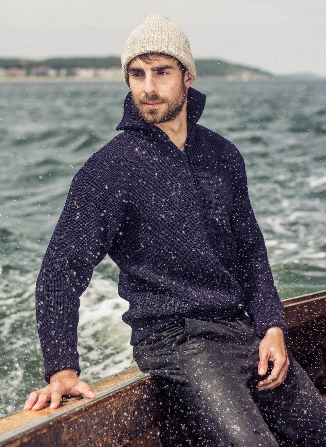 Mann im marineblauen Seemanns-Troyer und heller Strickmütze von Blauer Peter auf einem Boot bei Wellengang