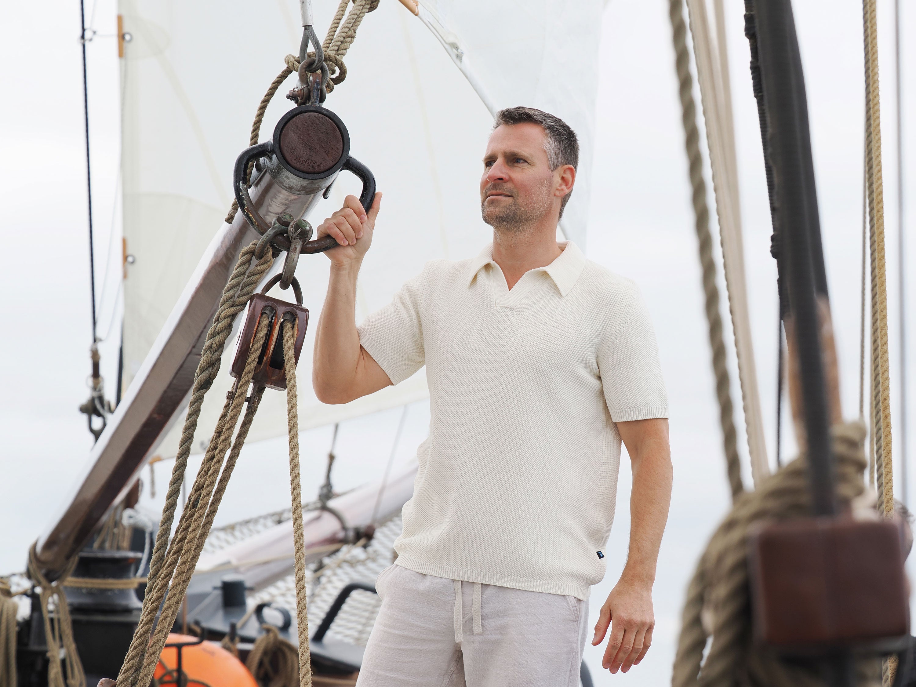 Mann trägt Strickpolo aus gasierter Baumwolle in Natur auf Schiff